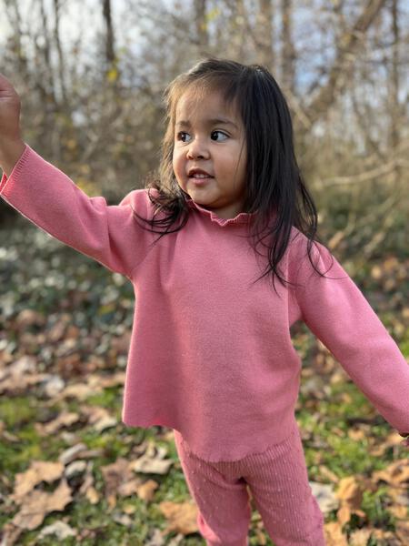 happy girl in autumn wood wearing pink cotton knit sweater with ruffle neck and matching leggings