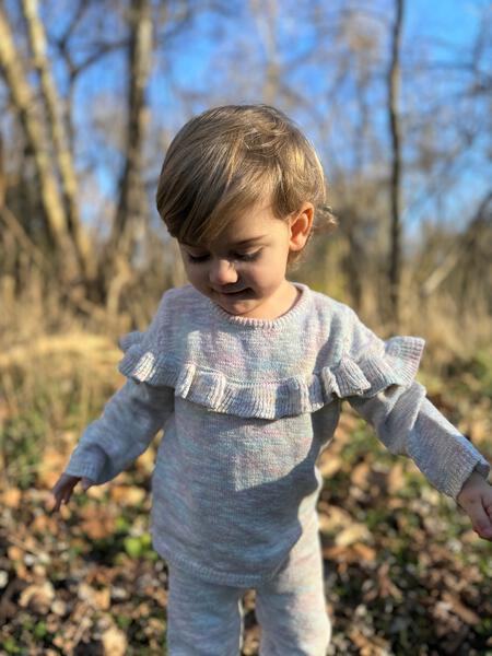 toddler in autumn woodland wearing knitted cotton sweater with frill shoulders and matching knit legging pants with side detail