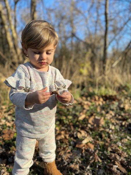 toddler in autumn woodland wearing knitted cotton sweater with frill shoulders and matching knit legging pants