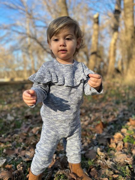 toddler in autumn woodland wearing knitted cotton sweater with frill shoulders and matching knit legging pants