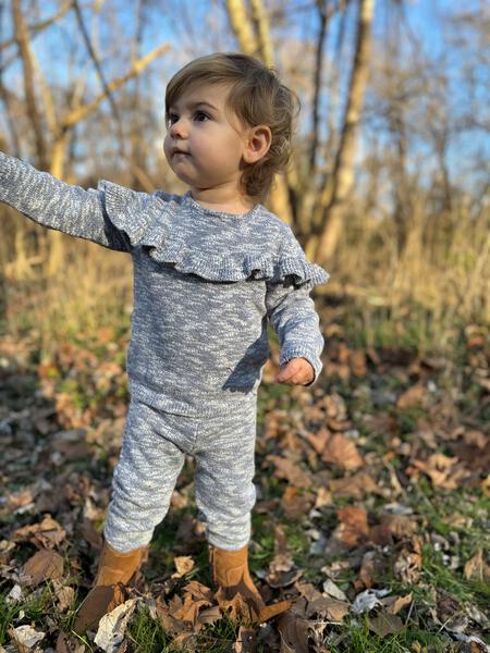 toddler in autumn woodland wearing knitted cotton sweater with frill shoulders and matching knit legging pants