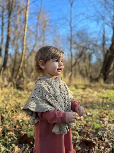 happy toddler in sunny autumn woods wearing oatmeal cotton knit lace poncho with wooden button and hood