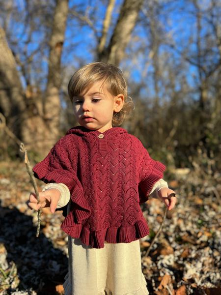 happy toddler in sunny autumn woods wearing rust cotton knit lace poncho with wooden button and hood