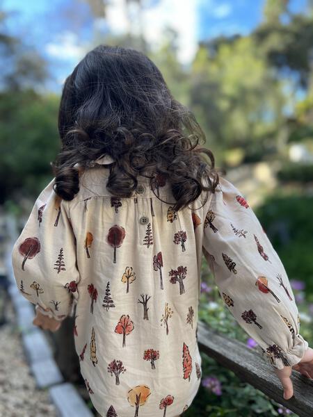 toddler in sunny garden wearing cream long sleeved bubble in tree print with peter pan collar