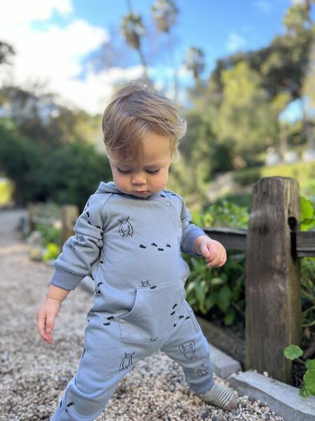 happy toddler in garden wearing long sleeved hooded romper with patch pocket and side zip fastening  in blue with yeti print