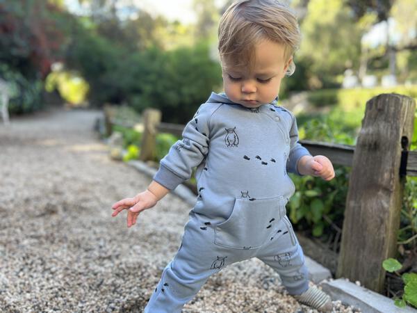 happy toddler in garden wearing long sleeved hooded romper with patch pocket and side zip fastening  in blue with yeti print