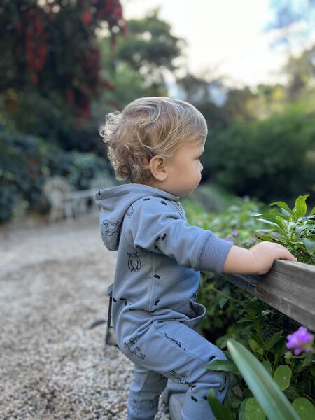 happy toddler in garden wearing long sleeved hooded romper with patch pocket and side zip fastening  in blue with yeti print