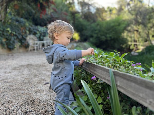 happy toddler in garden wearing long sleeved hooded romper with patch pocket and side zip fastening  in blue with yeti print