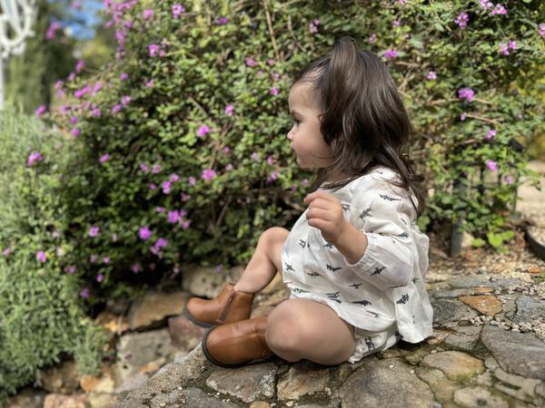 toddler in garden in sunshine wearing white short dress with matching bloomers in all over airplane print