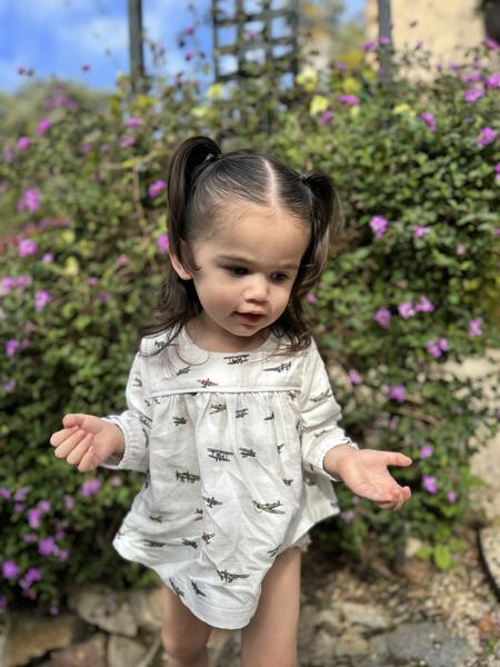 toddler in garden in sunshine wearing white short dress with matching bloomers in all over airplane print