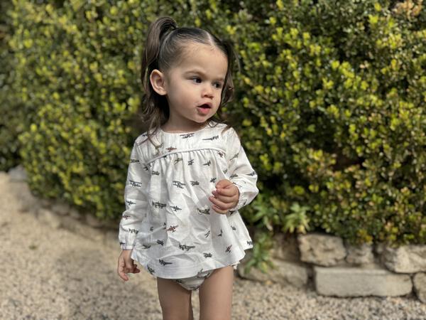 toddler in garden in sunshine wearing white short dress with matching bloomers in all over airplane print