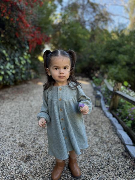 toddler standing in sunny autumn garden wearing green long sleeved jersey rib dress. buttons down the front