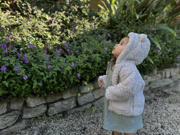 Toddler in garden wearing grey fleece fluffy jacket with bear ears on hood two patch pockets