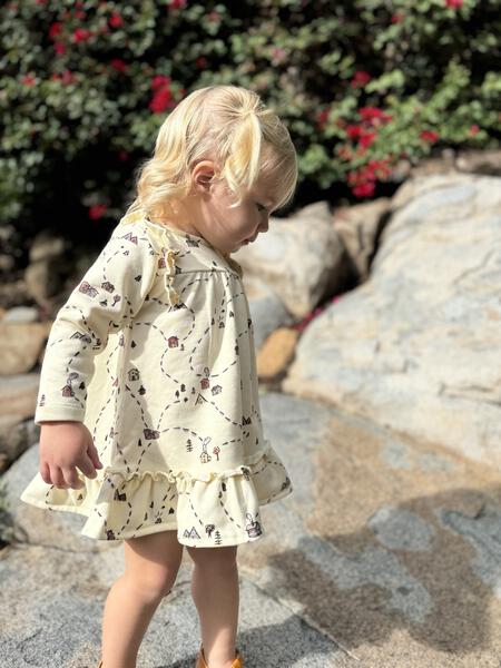 toddler standing in autumn sunshine wearing jersey dress with frill shoulders and hem with village map print all over