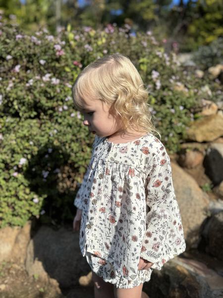 happy toddler in sunny garden wearing short dress in flower print with matching diaper cover pants