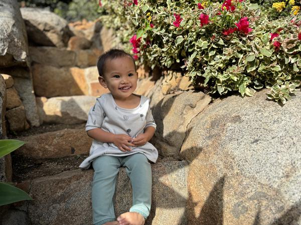 happy toddler sitting in autumn sunshine wearing green leggings and grey yeti print dress with 3/4 length sleeves a-line with side patch pockets