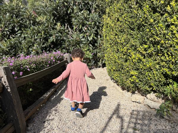 toddler in garden wearing pink long sleeved dress with lace trim on hem 