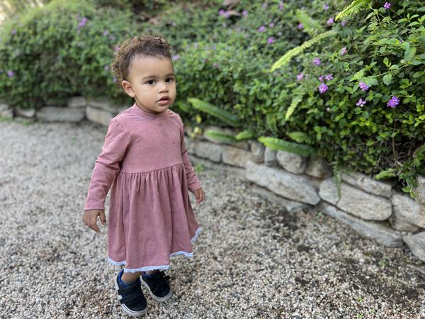 toddler in garden wearing pink long sleeved dress with lace trim on hem 