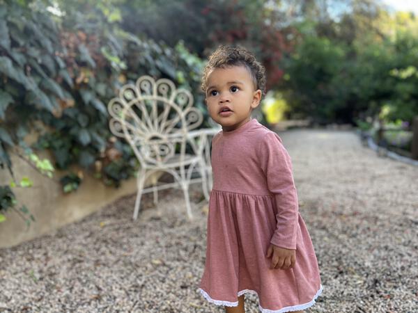 toddler in garden wearing pink long sleeved dress with lace trim on hem 