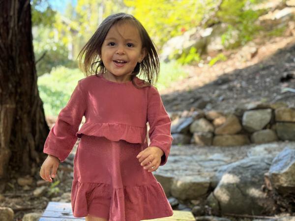 happy girl in autumn sunshine in woods wearing berry red long sleeved dress with frill at waist and hem 