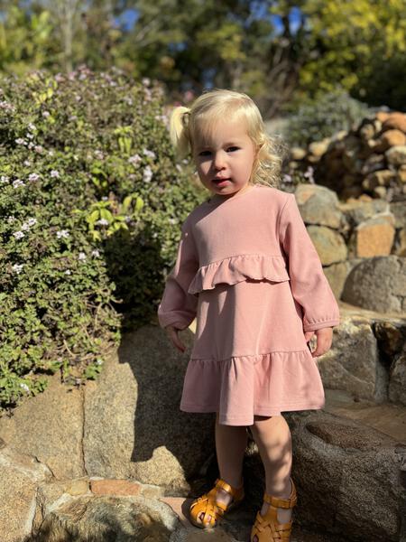 happy toddler in autumn sunshine wearing pink long sleeved dress with frill at waist and hem