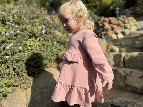 happy toddler in autumn sunshine wearing pink long sleeved dress with frill at waist and hem 