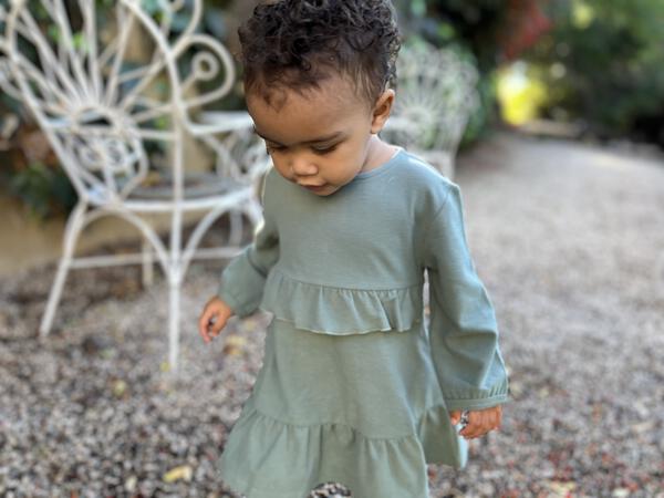 happy toddler in autumn sunshine wearing green long sleeved dress with frill at waist and hem