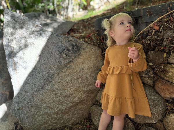 happy toddler in autumn sunshine wearing gold long sleeved dress with frill at waist and hem