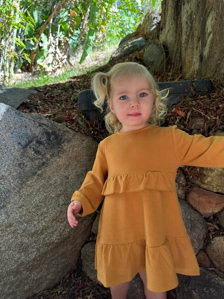 happy toddler in autumn sunshine wearing gold long sleeved dress with frill at waist and hem