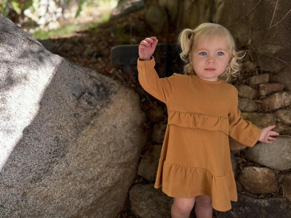 happy toddler in autumn sunshine wearing gold long sleeved dress with frill at waist and hem