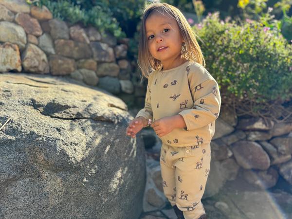 happy girl in sunny garden wearing sweat top in beige with woodland critters print back opening and matching sweat pants