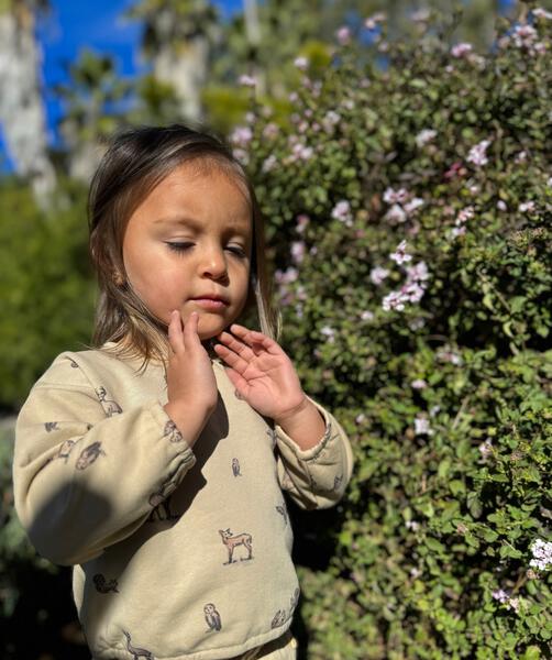 happy girl in sunny garden wearing sweat top in beige with woodland critters print back opening and matching sweat pants