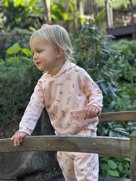 toddler in autumn sunshine wearing pink hooded sweat top with patch pocket and all over flower print and matching sweat pants with side patch pockets