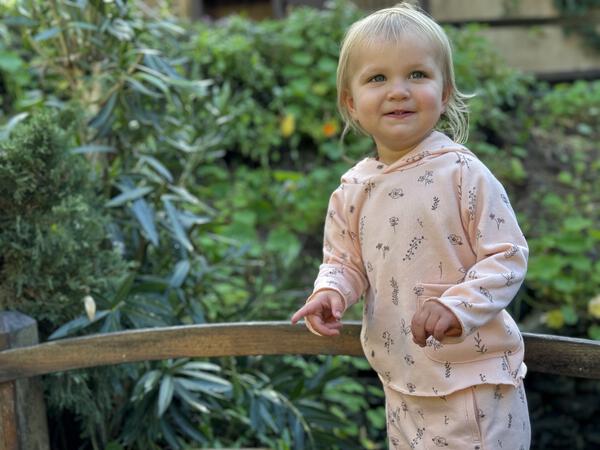 toddler in autumn sunshine wearing pink hooded sweat top with patch pocket and all over flower print and matching sweat pants with side patch pockets