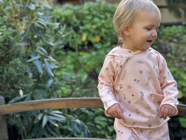 toddler in autumn sunshine wearing pink hooded sweat top with patch pocket and all over flower print and matching sweat pants with side patch pockets