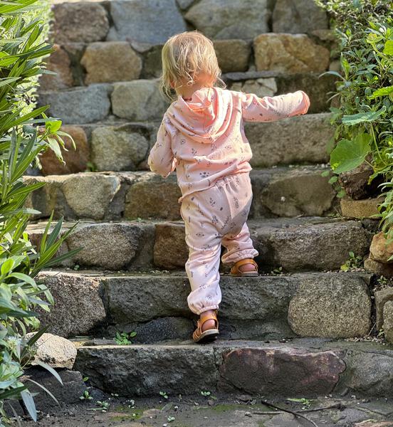 toddler in autumn sunshine wearing pink hooded sweat top with patch pocket and all over flower print and matching sweat pants with side patch pockets