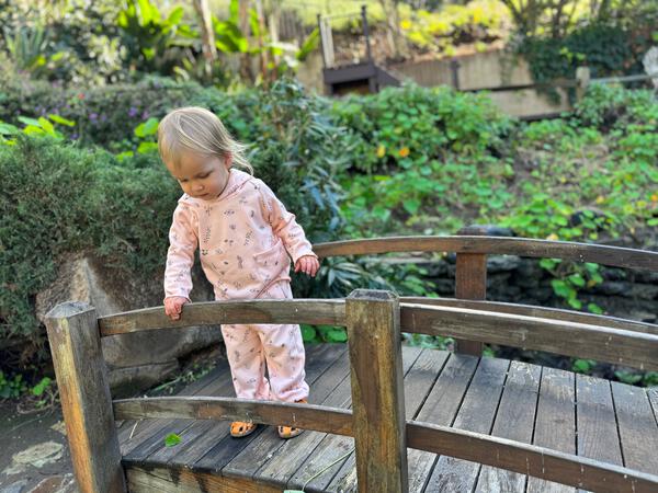 toddler in autumn sunshine wearing pink hooded sweat top with patch pocket and all over flower print and matching sweat pants with side patch pockets