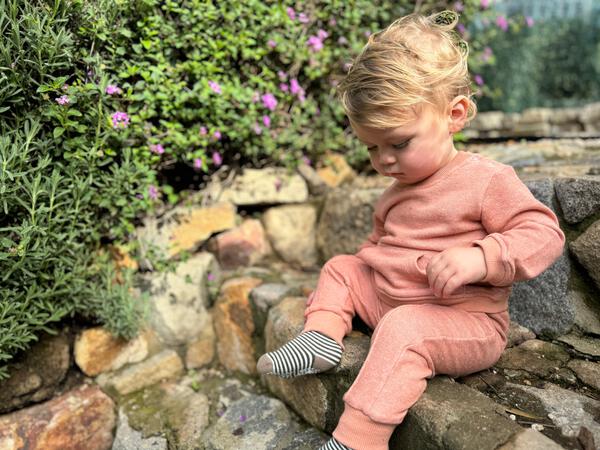 toddler sat on old stone wall wearing rust sweat pants with side pickets and front line detail and matchiing swaet shirt