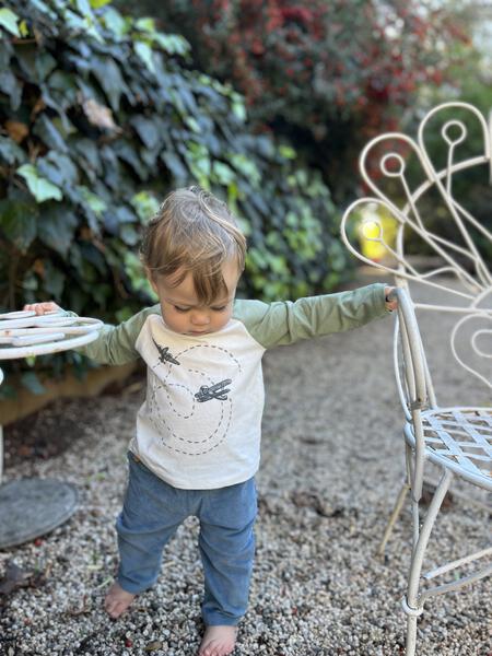 happy toddler in garden wearing blue cord pants with patch pockets and button detail and airplane print tee