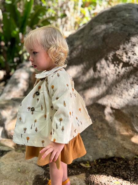 toddler in sunshine wearing cord jacket with double breasted buttons and peter pan collar cream tree print