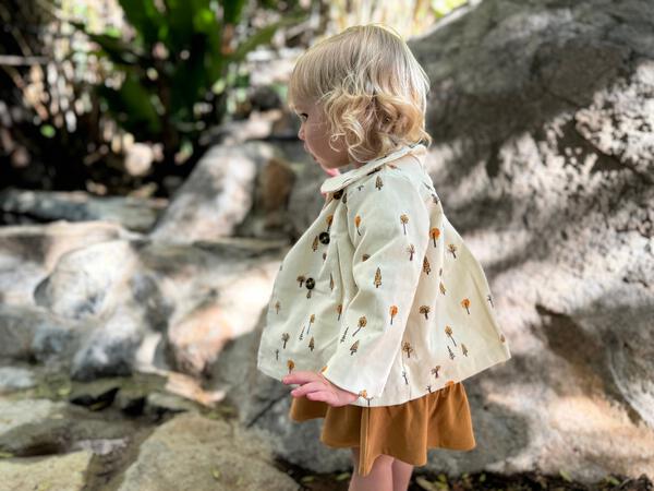 toddler in sunshine wearing cord jacket with double breasted buttons and peter pan collar cream tree print