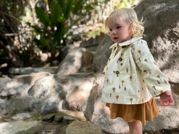 toddler in sunshine wearing cord jacket with double breasted buttons and peter pan collar cream tree print