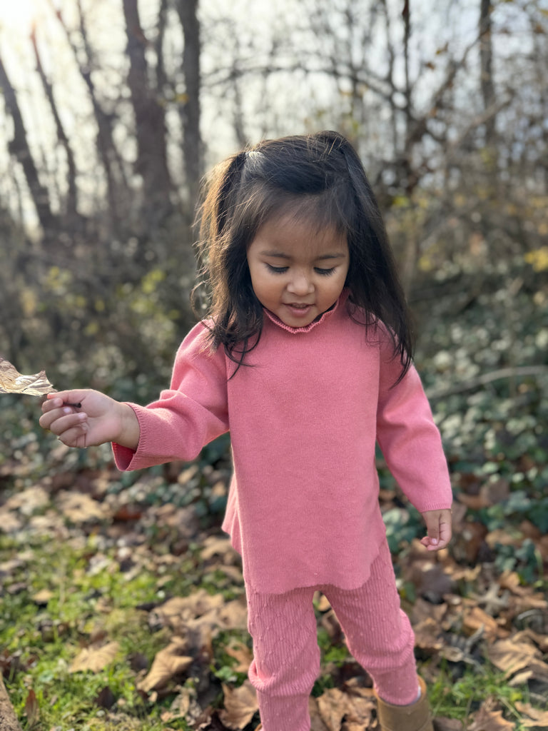 happy girl in autumn wood wearing pink cotton knit sweater with ruffle neck and matching leggings