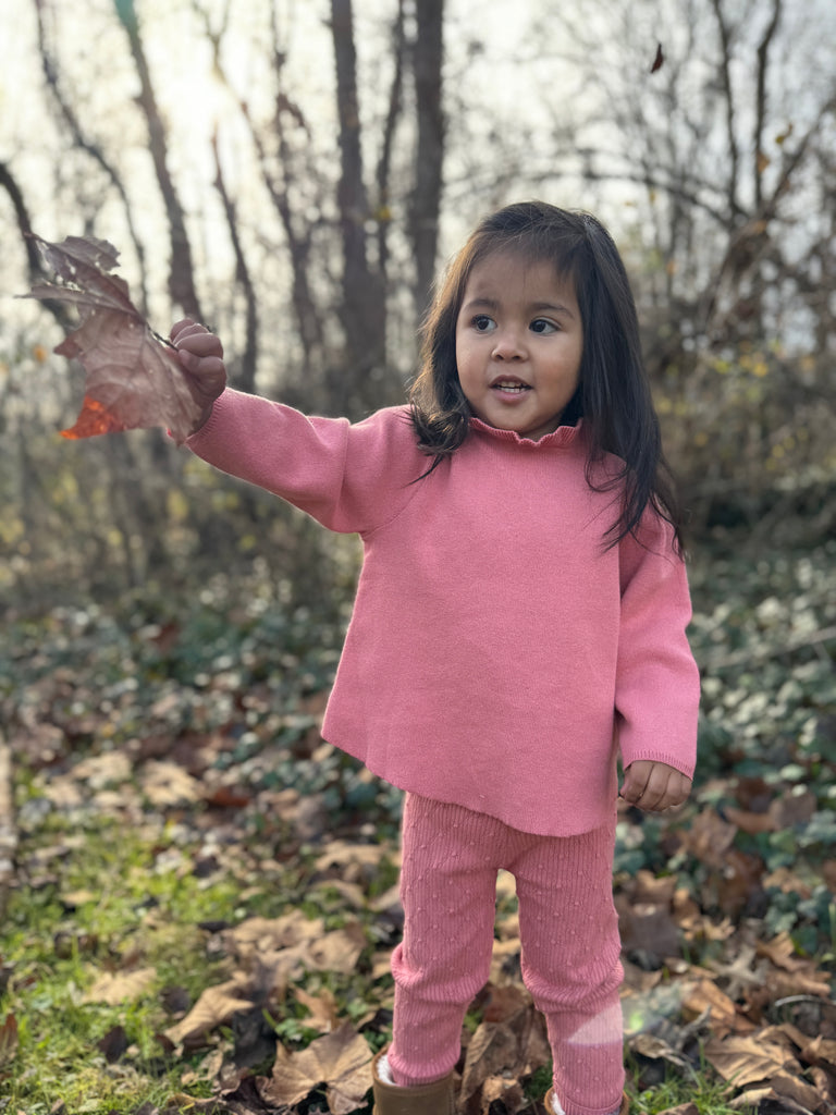 happy girl in autumn wood wearing pink cotton knit sweater with ruffle neck and matching leggings