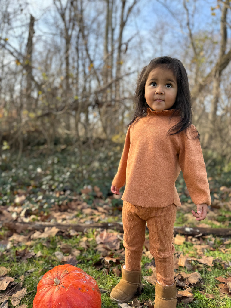 girl in autumnal wood wearing gold patterned knit leggings and matching  knitted sweater