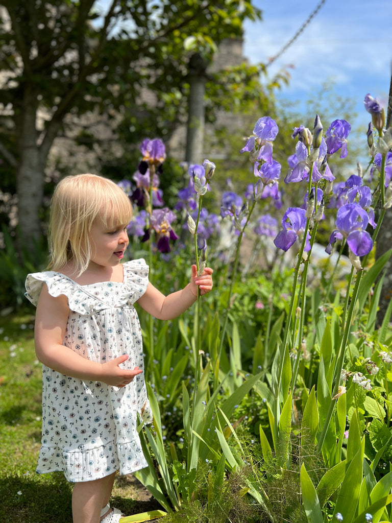 girl standing in summer garden flowers on sunny day wearing white dress with flower print frill shoulders hem frill