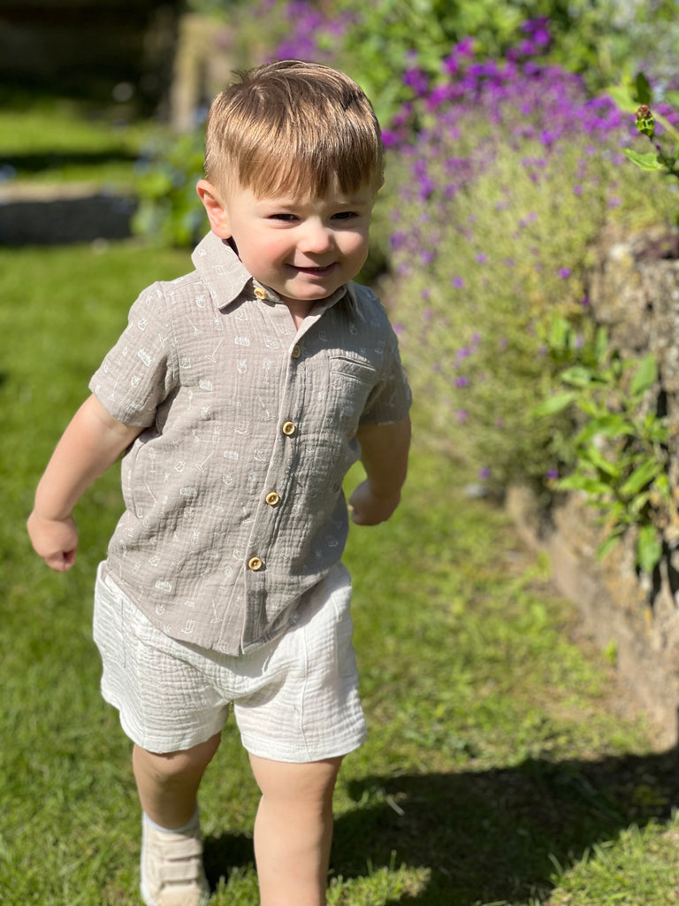 boy in sunny garden wearing white gauze shorts with side patch pockets and elasticated waist and grey shirt