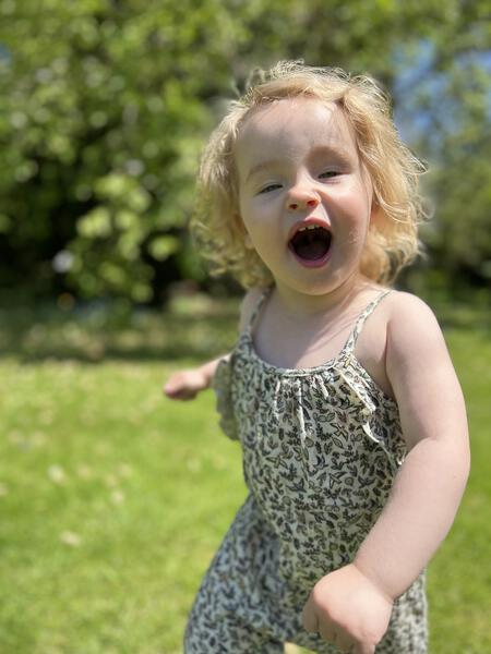 happy toddler running in sunny garden wearing  jersey long legged romper with shoe string straps and frills Small flowers and birds print on cream background