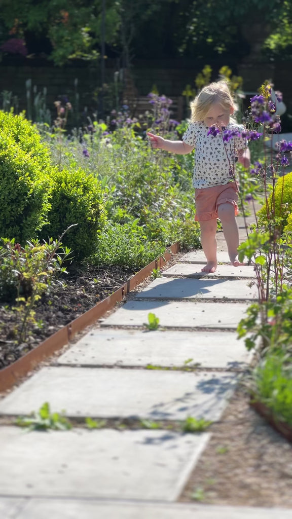 happy girl skipping down sunny garden path wearing tee shirt in white ribbed jersey with seahorse print and coral shorts