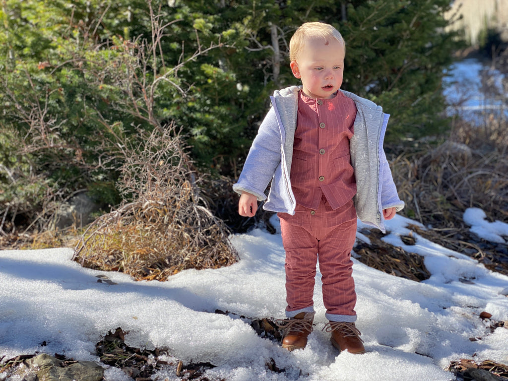 toddler standing in snowy wood wearing padded jacket zip front with hood grey jersey with tree print lining